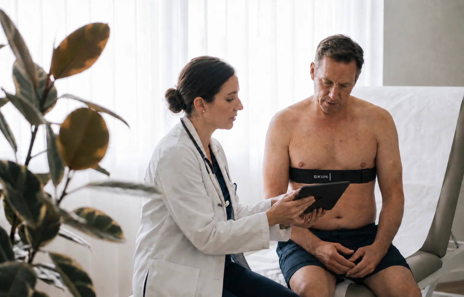 A physician showing a patient their recording on a tablet, the patient wearing the SKIIN chest band