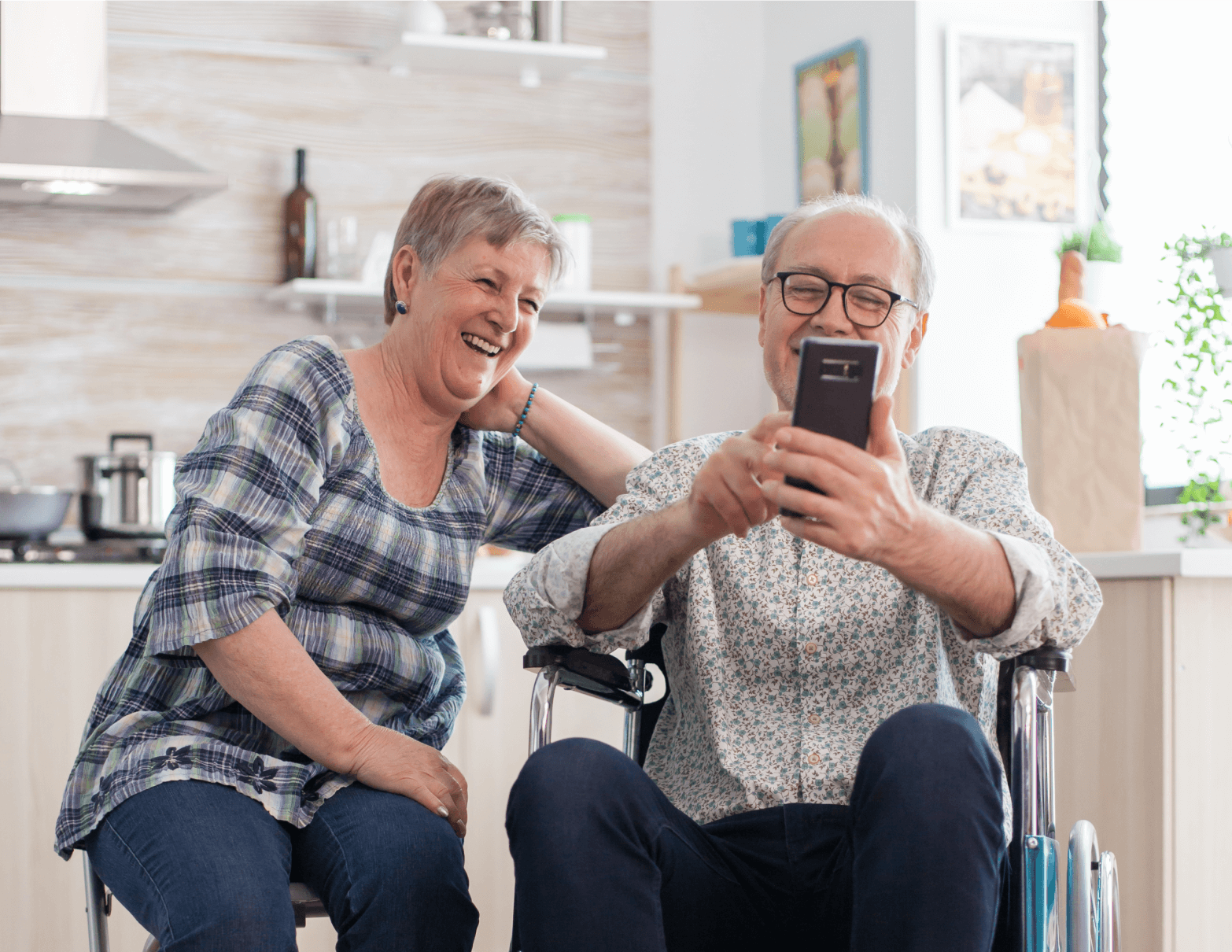 disabled-senior-man-wheelchair-his-wife-laughing-browsing-with-modern-smartphone-kitchen-paralyzed-old-man-his-wife-having-online-conference 1 (5) (1)